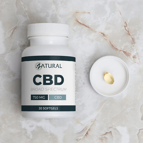 CBD supplement bottle labeled 'Natural' on a marble surface with a softgel capsule.