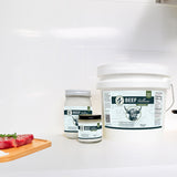 Three containers of beef tallow on a white surface with a wooden cutting board.