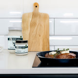 Two jars labeled 'Beef Fellow' on a kitchen counter with a pan of food and a cutting board.