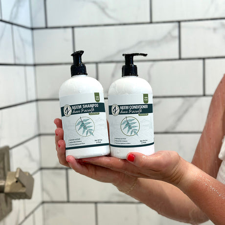 Two bottles of Neem Shampoo and Conditioner held in front of a tiled shower wall.