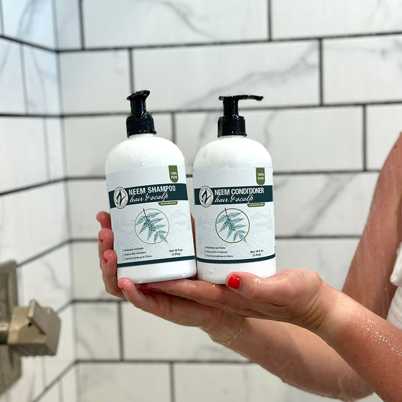 Two bottles of Neem Shampoo and Conditioner held in front of a tiled shower wall.