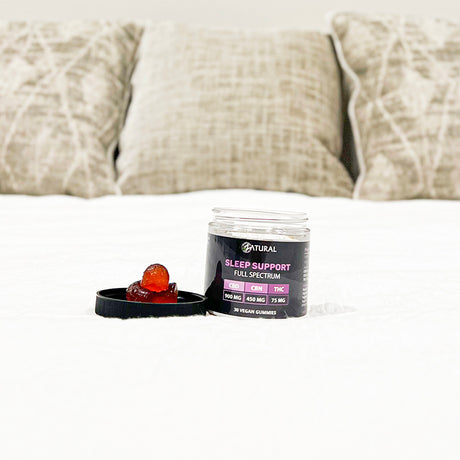 Sleep support gummies and container on a bed with pillows in the background